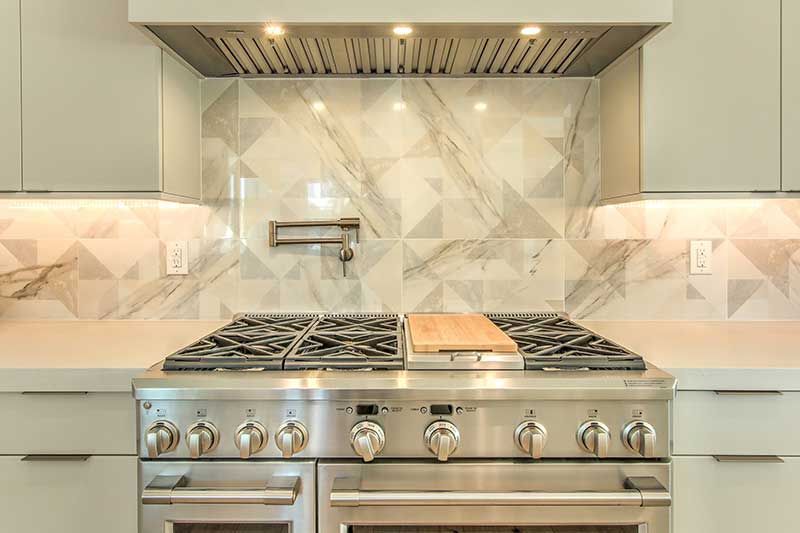 Modern kitchen with a stainless steel stove, geometric marble backsplash, and a wooden cutting board on the countertop.